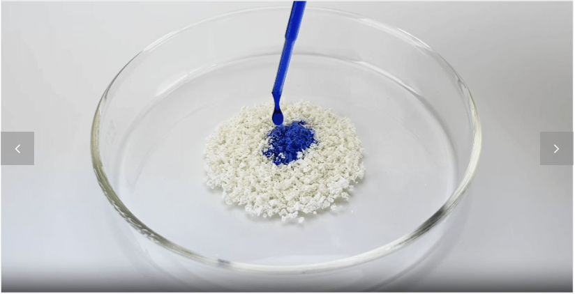 White granules in a glass dish with blue liquid being applied.
